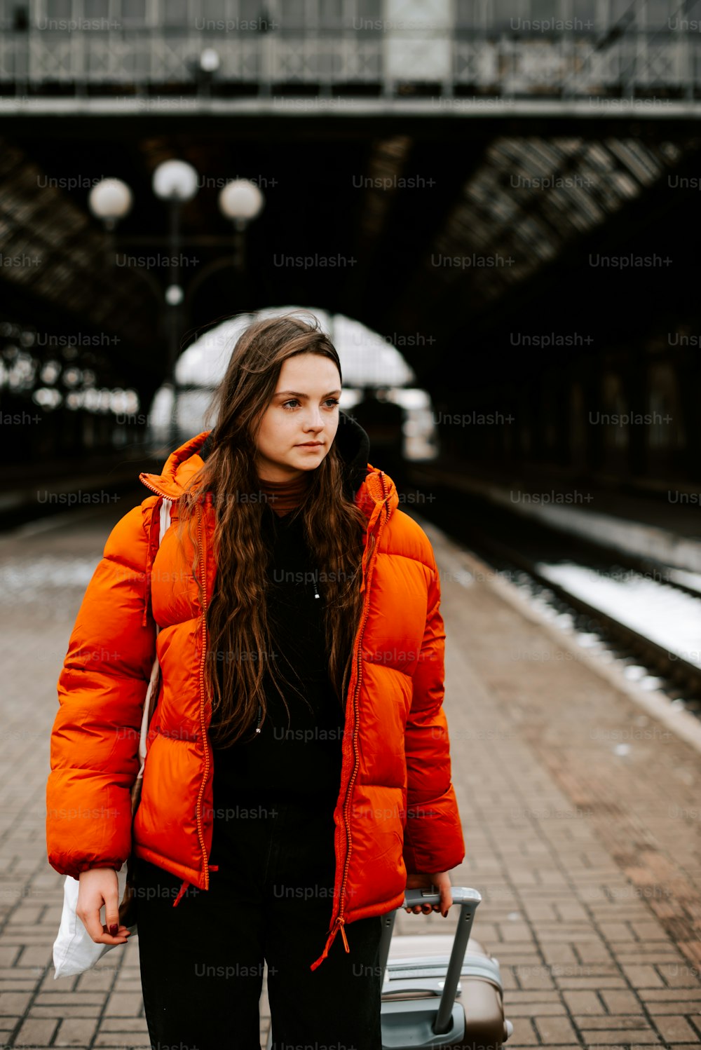 a woman in an orange puffer jacket is holding a suitcase