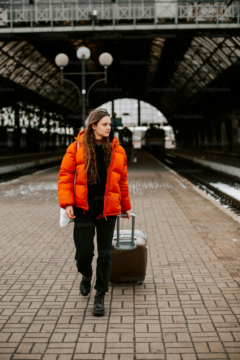 a woman in an orange jacket carrying a suitcase