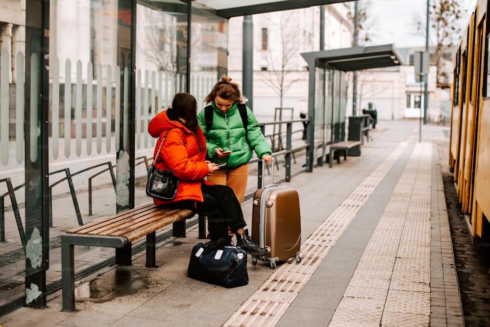two women sitting on a bench with their luggage