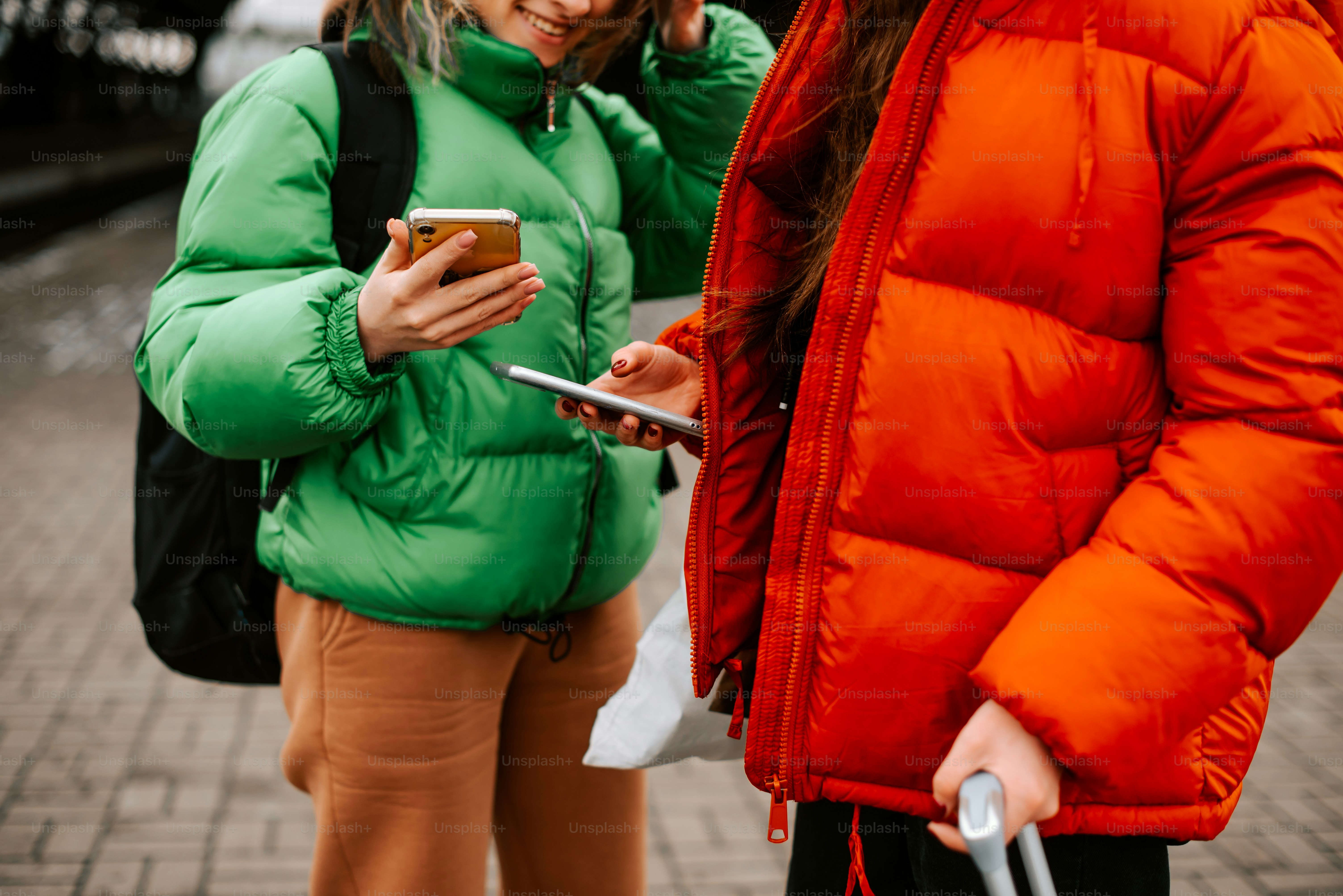 Dos mujeres de pie una al lado de la otra mirando sus teléfonos celulares