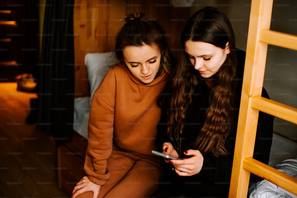 two girls sitting on a bunk bed looking at a cell phone