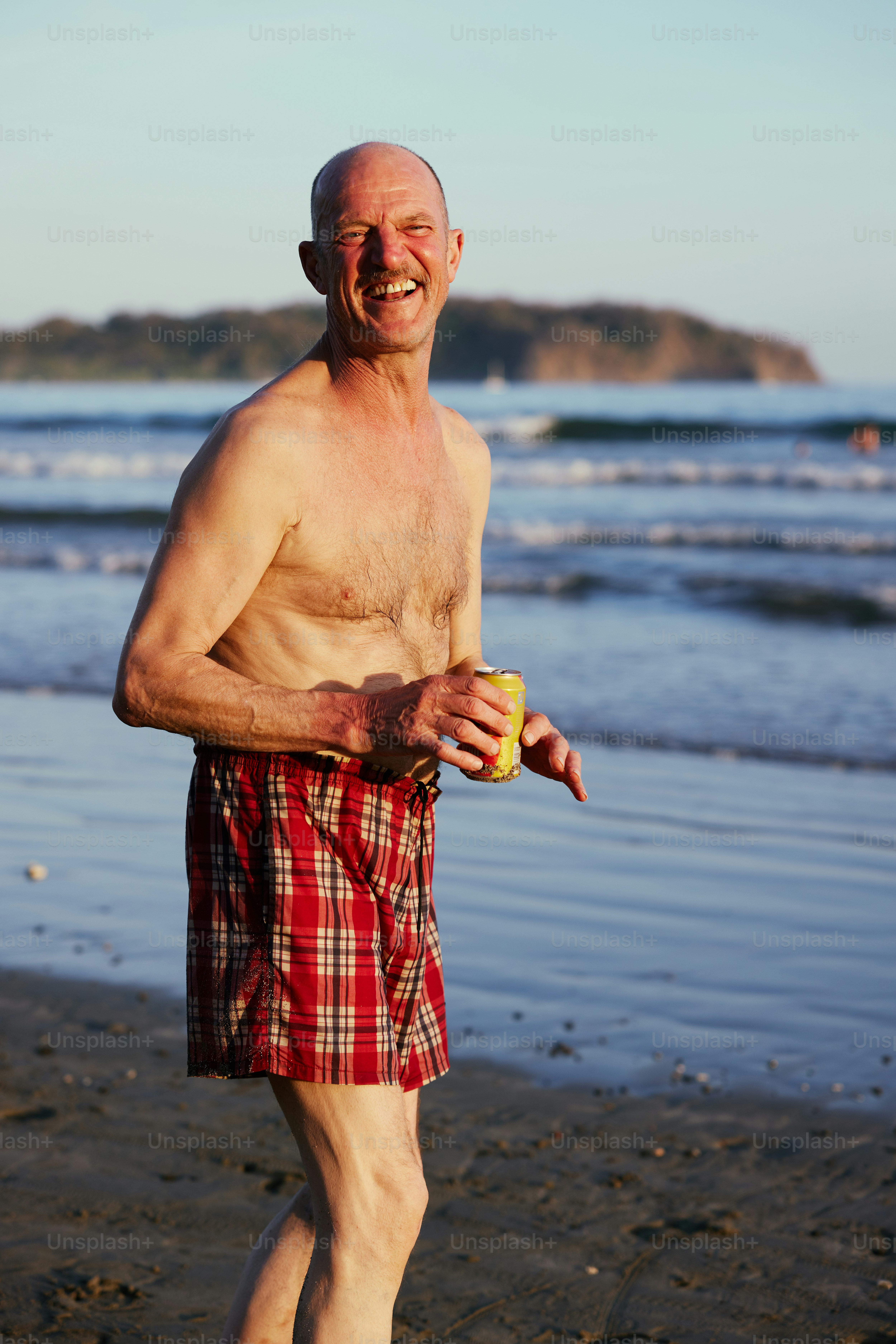 an older man standing on a beach holding a frisbee