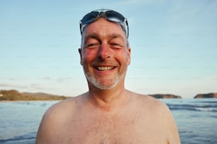 a man with no shirt wearing sunglasses on a beach