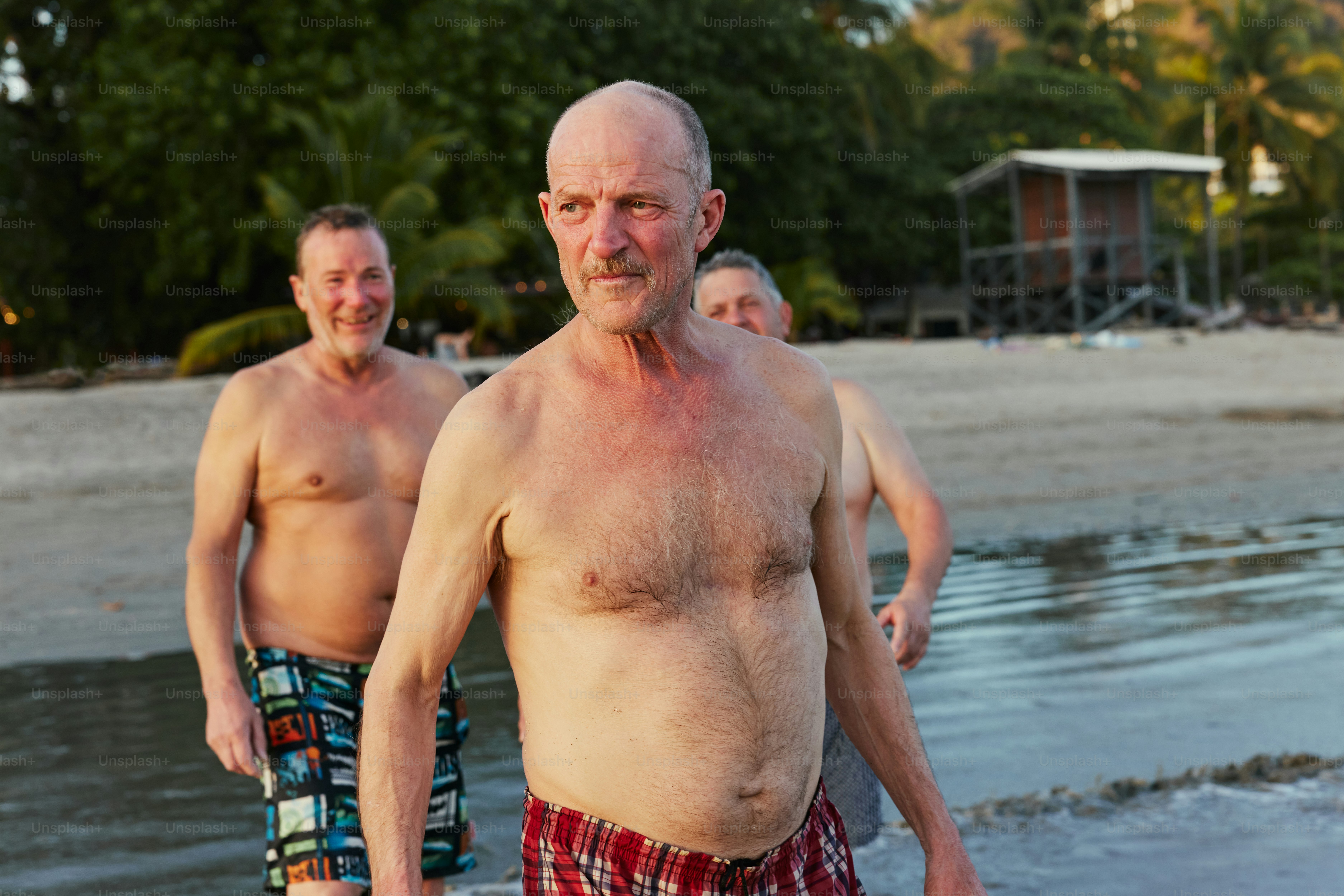 a man without a shirt on a beach next to another man