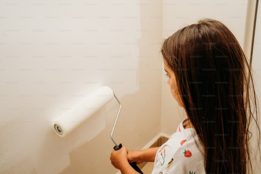 a young girl painting a wall with a roller