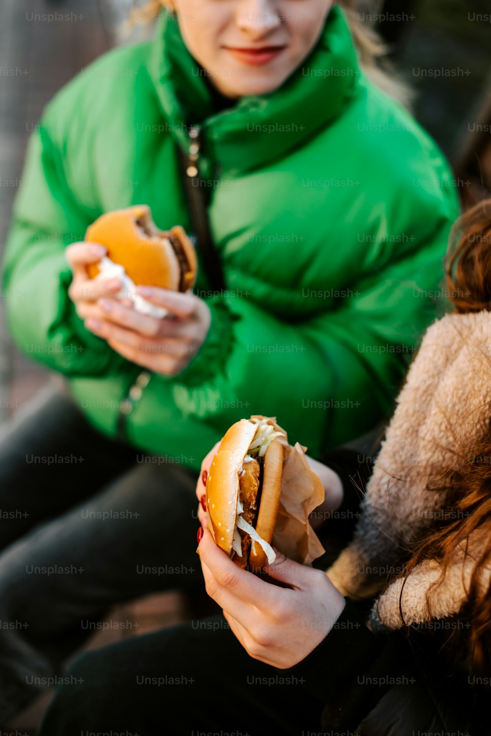 a woman in a green jacket eating a hot dog