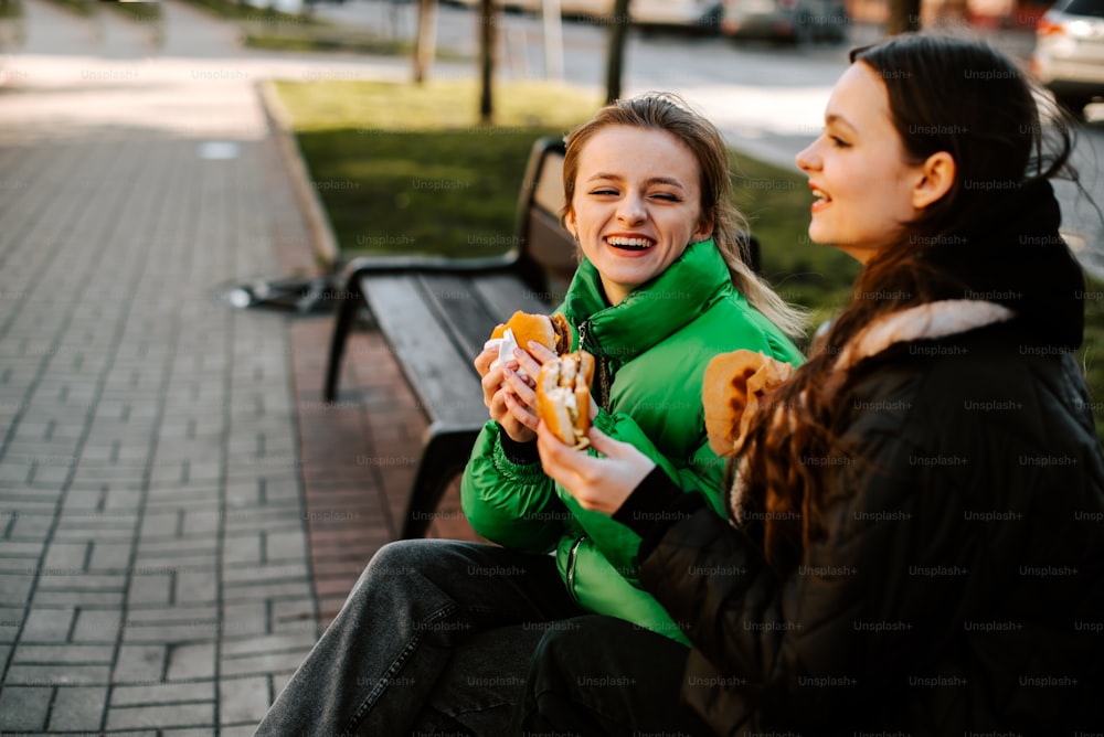 two women sitting on a bench eating food