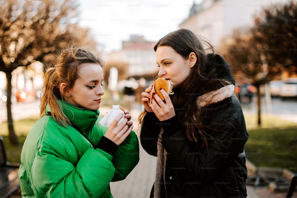 two women eating hot dogs on a city street