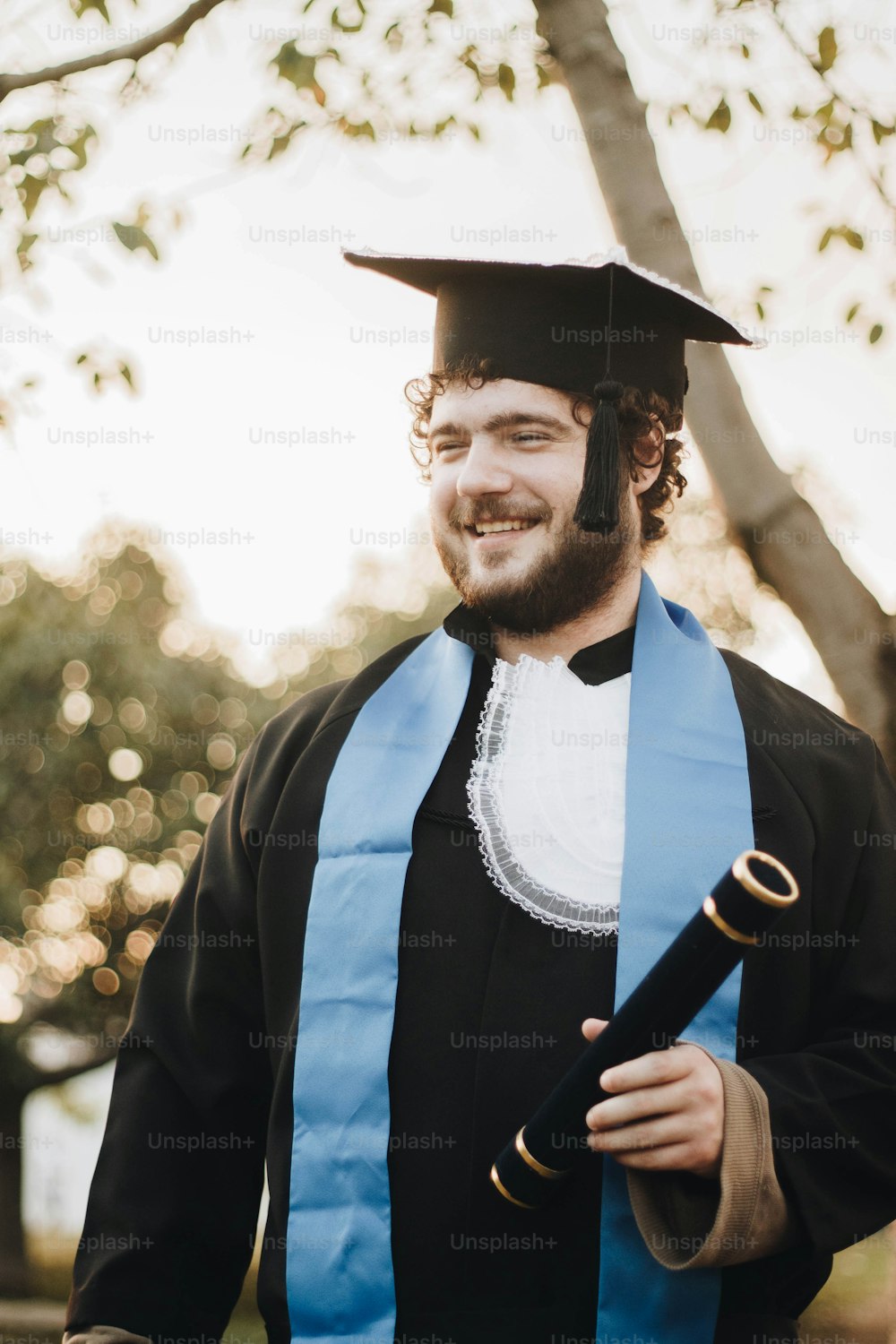 Ein Mann mit Mütze und Gewand, der ein Diplom in der Hand hält