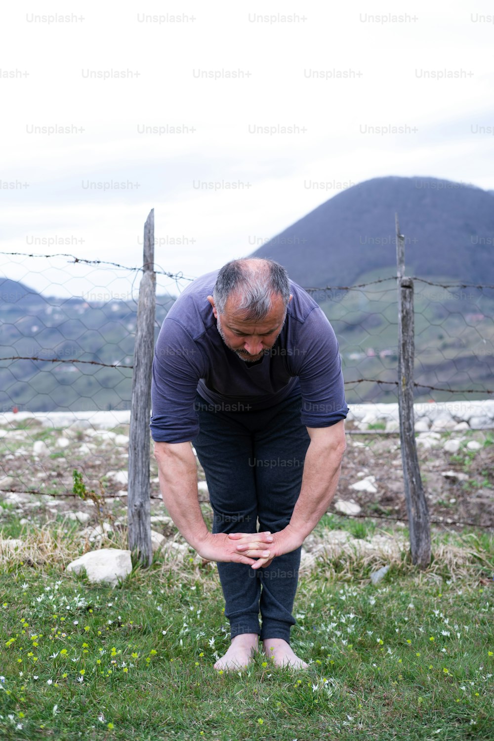 a man bending over in a field with mountains in the background