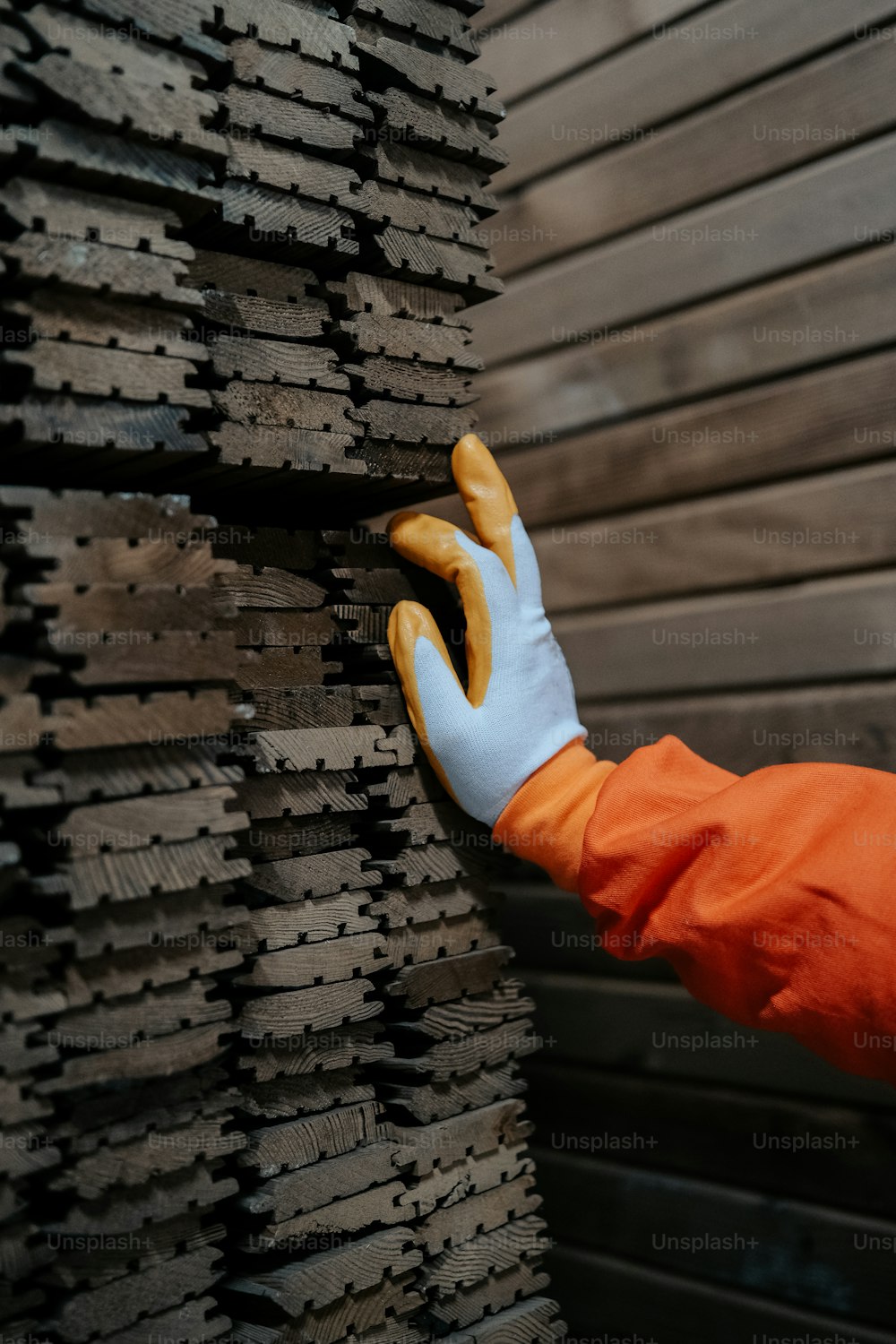 a person in an orange jacket and white glove holding onto a stack of wooden plank