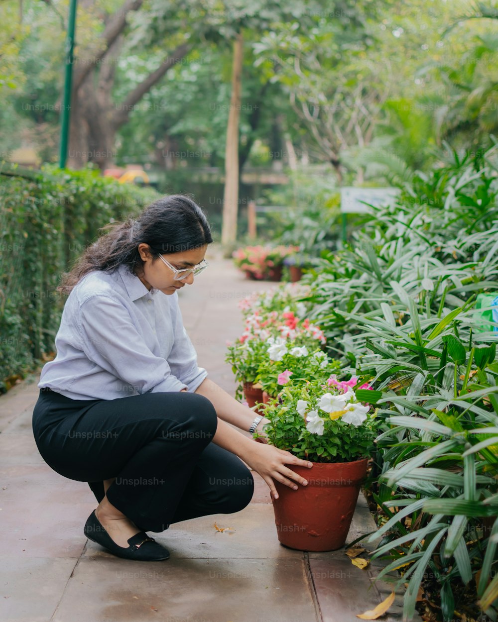 a woman kneeling down next to a potted plant