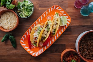 two tacos on an orange plate next to bowls of rice and vegetables