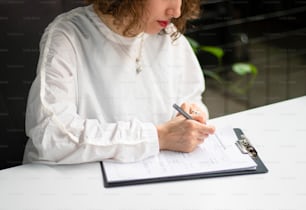 Eine Frau sitzt an einem Tisch und schreibt auf ein Blatt Papier