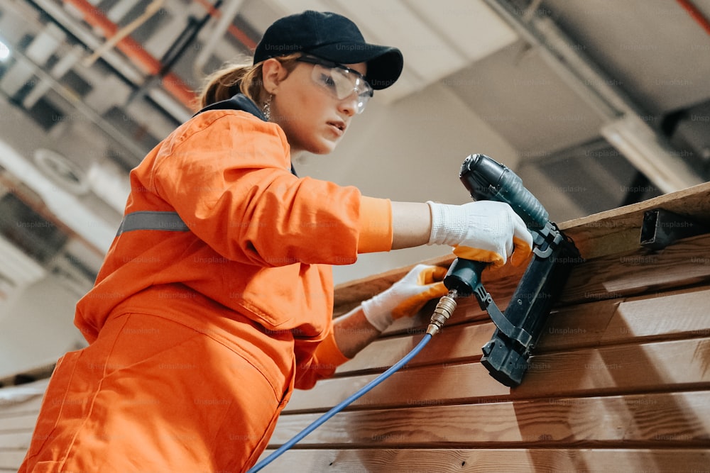 Eine Frau in einem orangefarbenen Overall, die an einem Stück Holz arbeitet