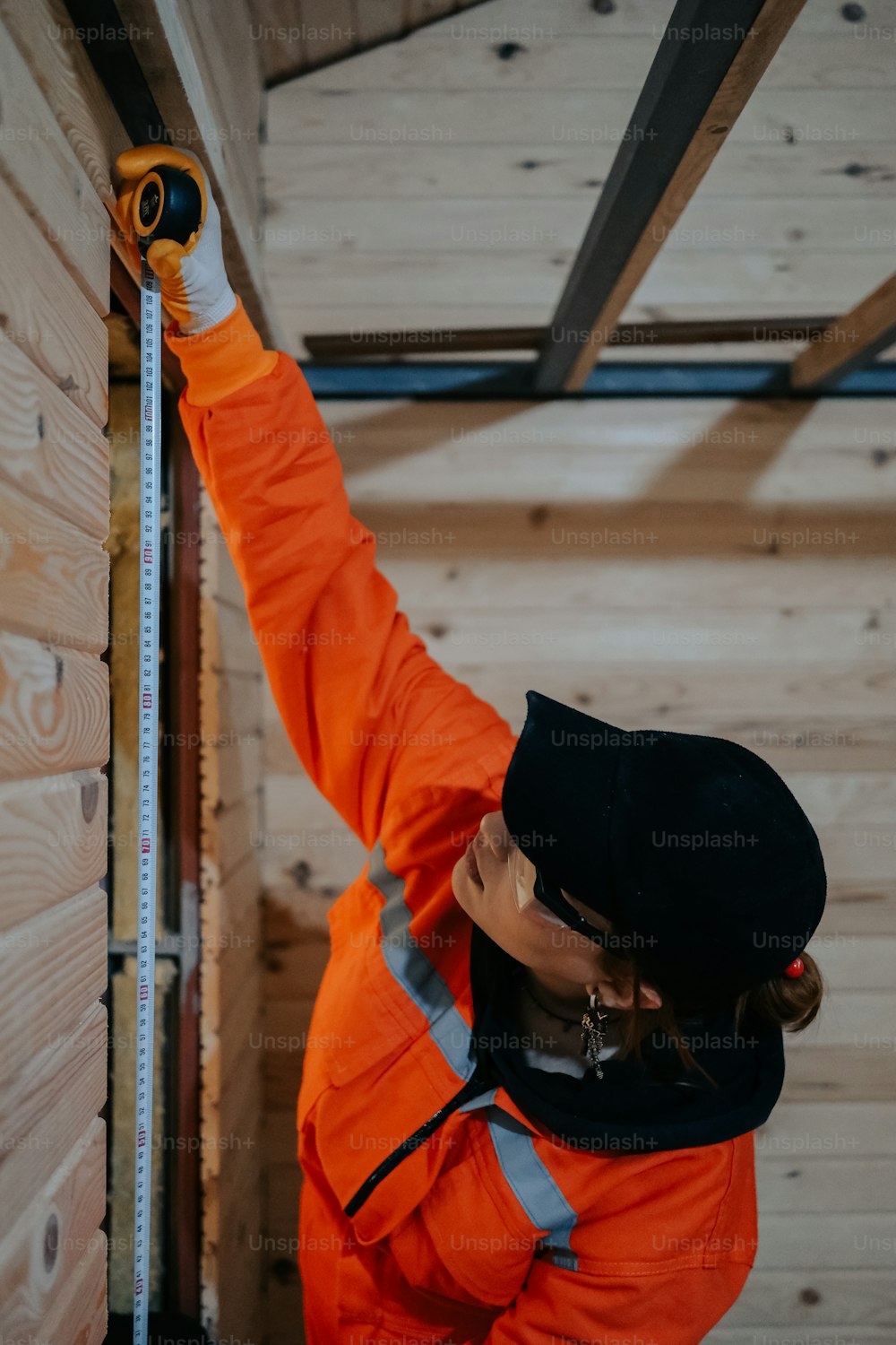 a woman in an orange jacket is measuring wood