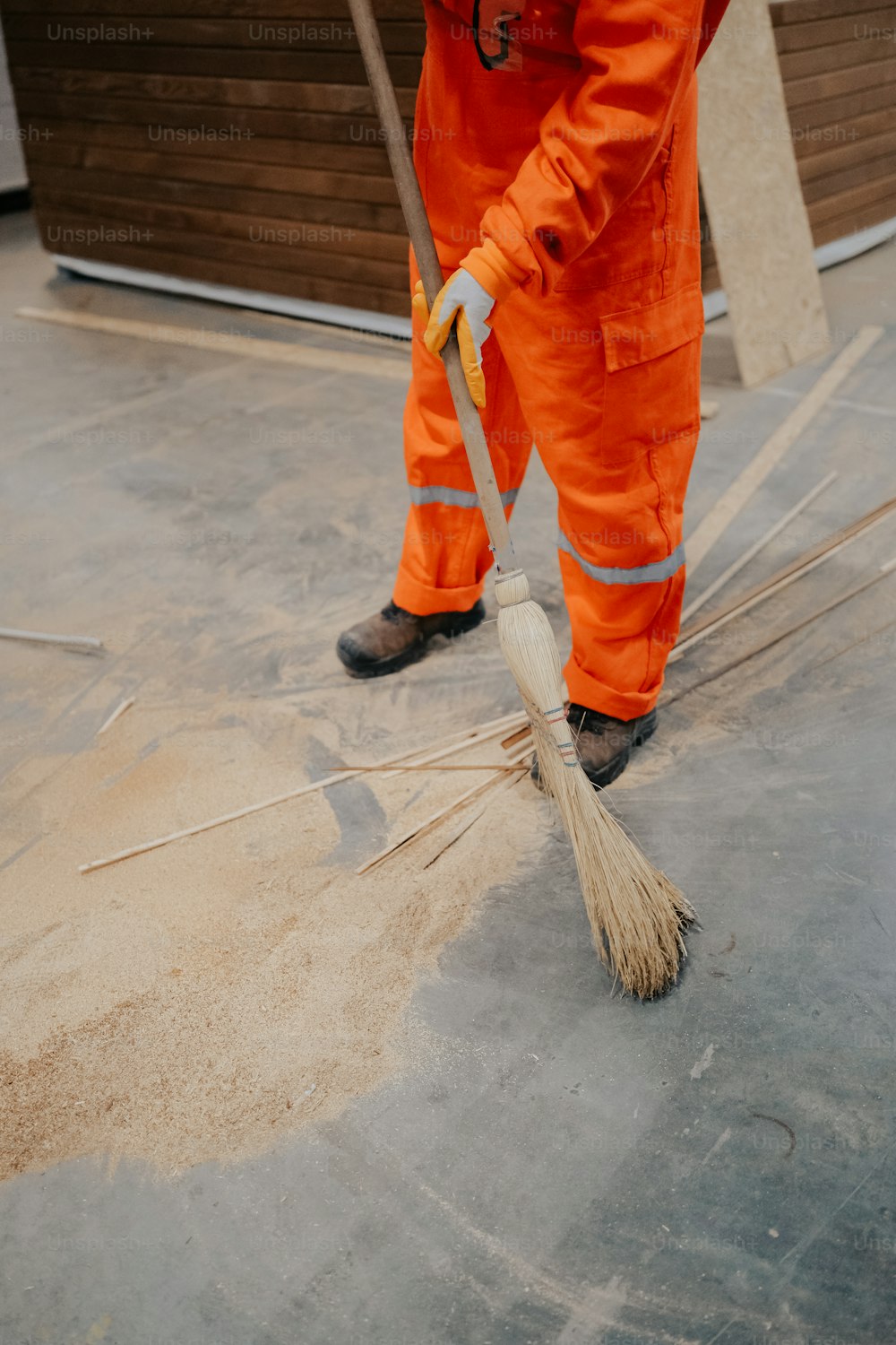 Un homme en combinaison orange nettoie le sol avec un balai
