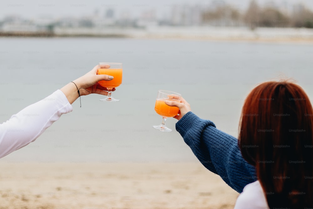 Zwei Frauen stoßen am Strand mit Orangensaft an