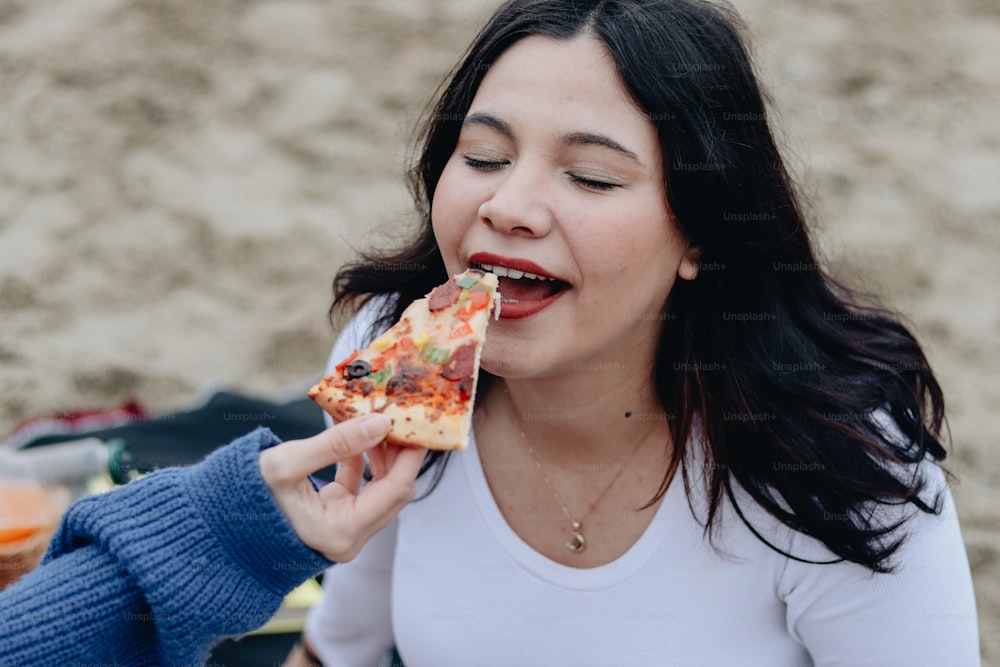 a woman eating a slice of pizza on the beach