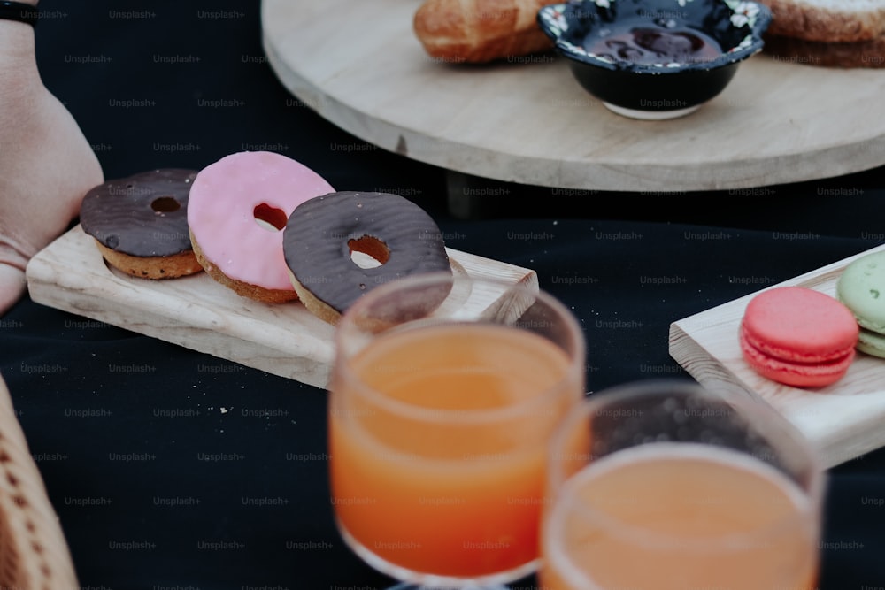 a wooden tray topped with donuts next to glasses of orange juice