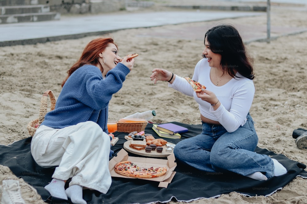 two women sitting on a blanket eating pizza