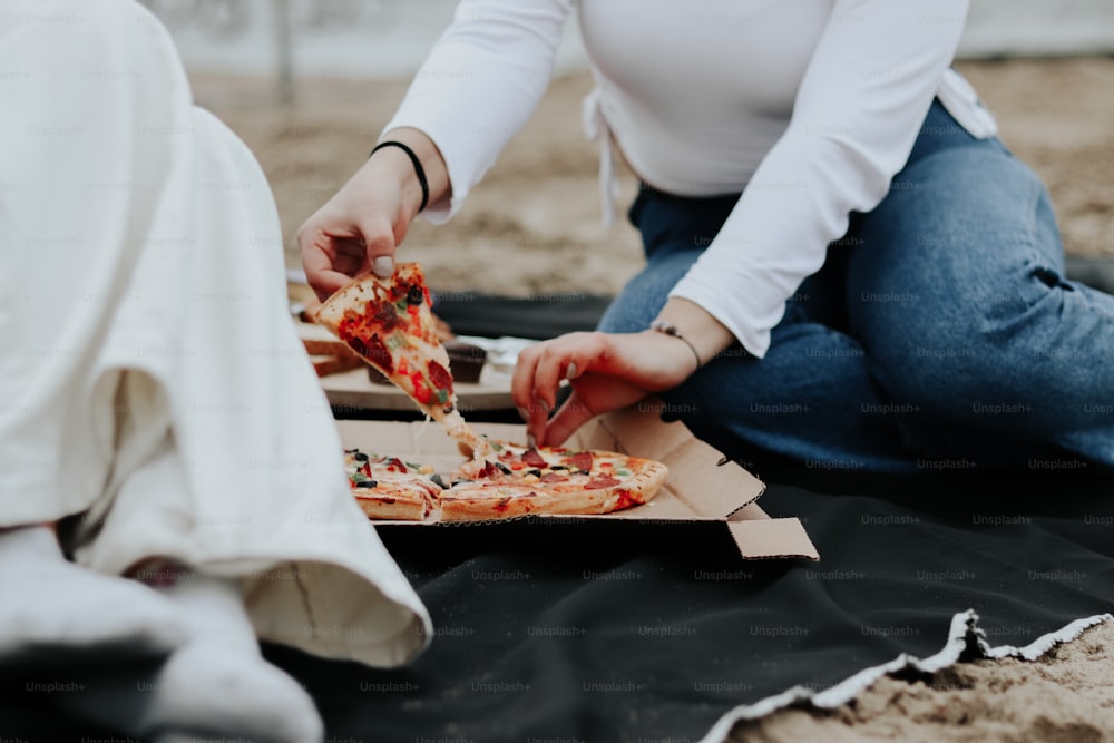 Una mujer sentada en el suelo comiendo una rebanada de pizza