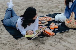 a woman sitting on a blanket on the beach reading a book