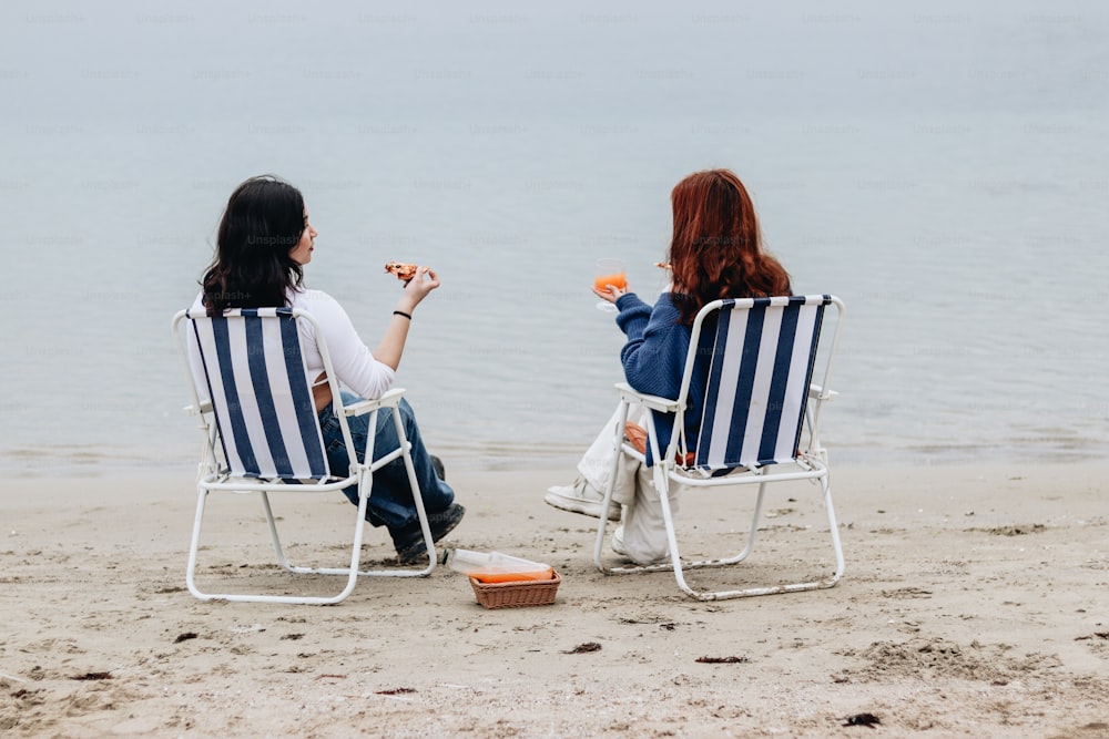 a couple of women sitting in lawn chairs on top of a beach