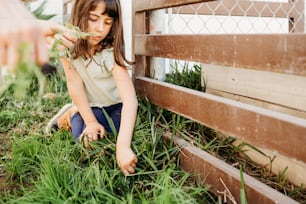 a little girl sitting on the ground next to a fence