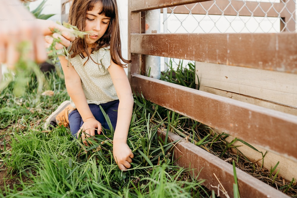 a little girl sitting on the ground next to a fence
