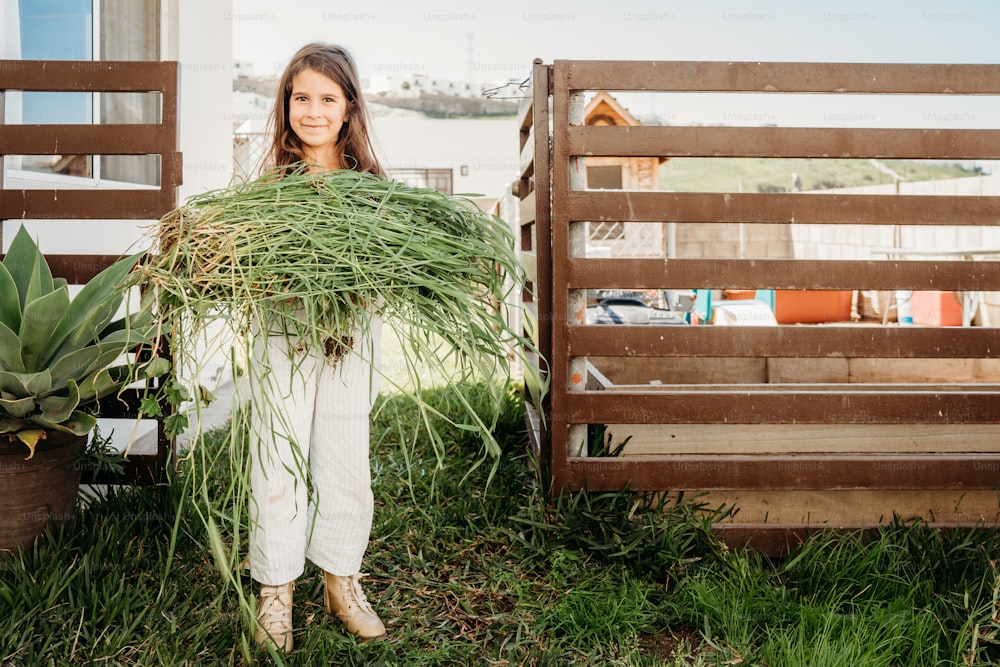 a woman holding a bunch of grass in front of a fence