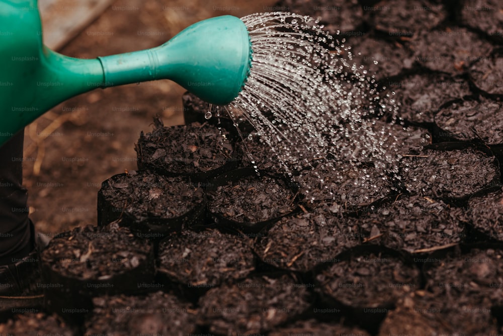 a person holding a green watering hose over a pile of dirt