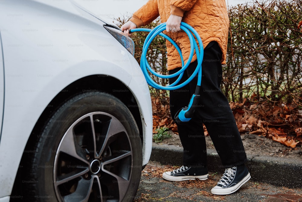 a man is holding a blue hose next to a white car