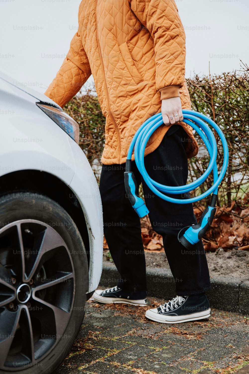 a man holding a blue hose next to a white car