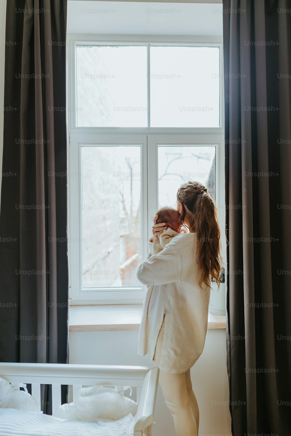 a woman standing in front of a window holding a baby