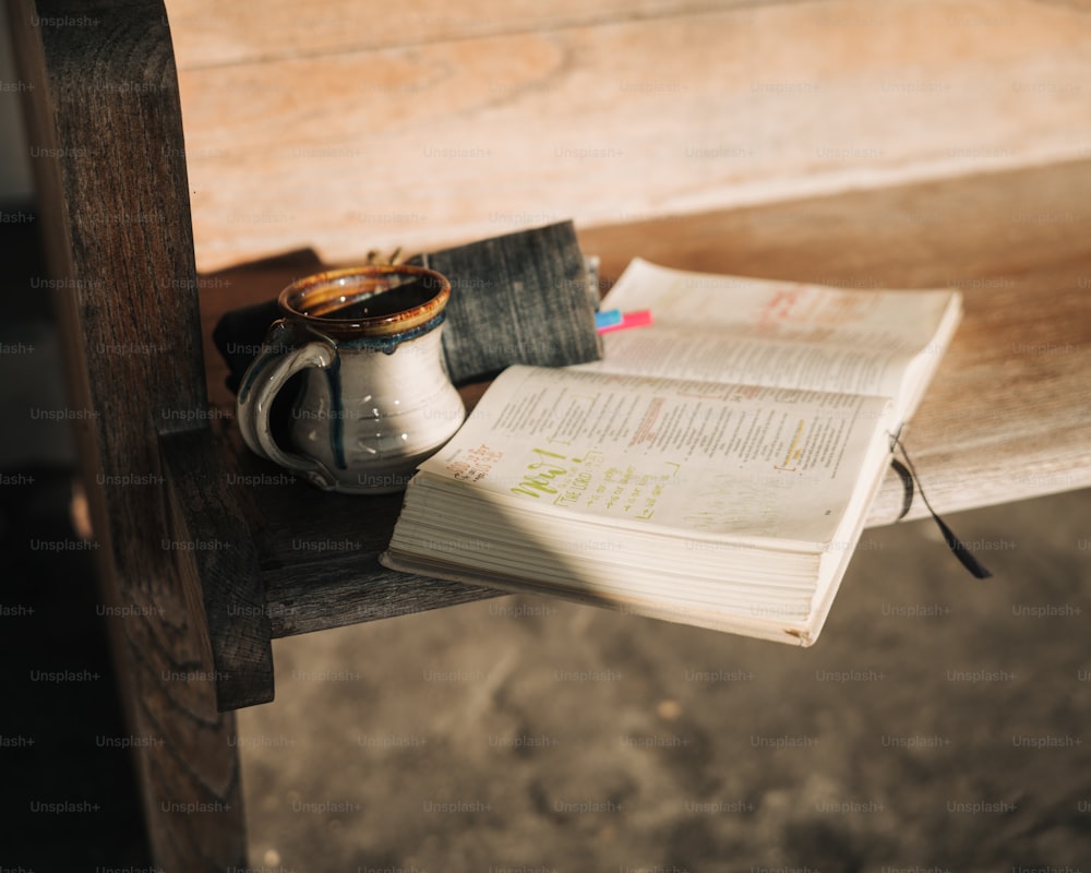 Un libro abierto y una taza en un banco