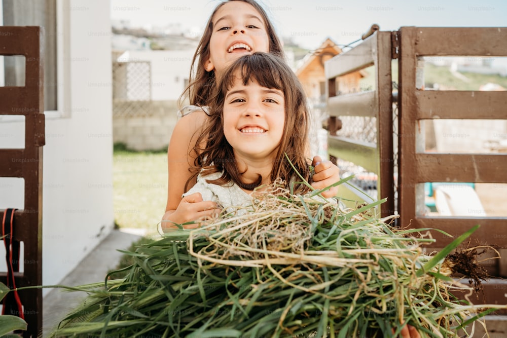 two young girls standing next to a pile of hay