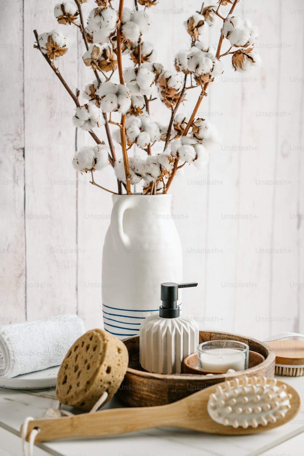 un vase blanc rempli de fleurs de coton à côté d’une brosse en bois