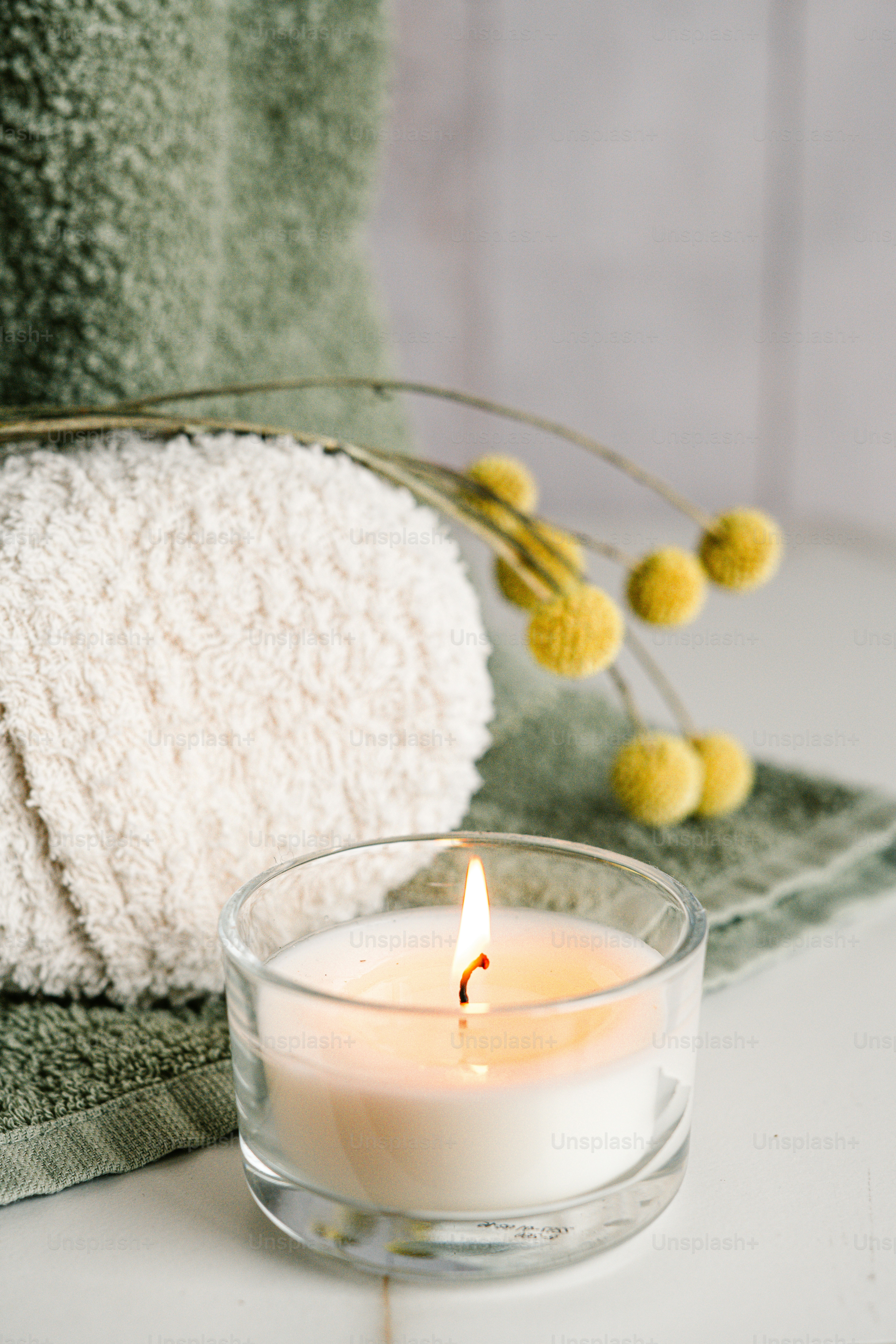 Una vela blanca sentada encima de una mesa junto a una toalla