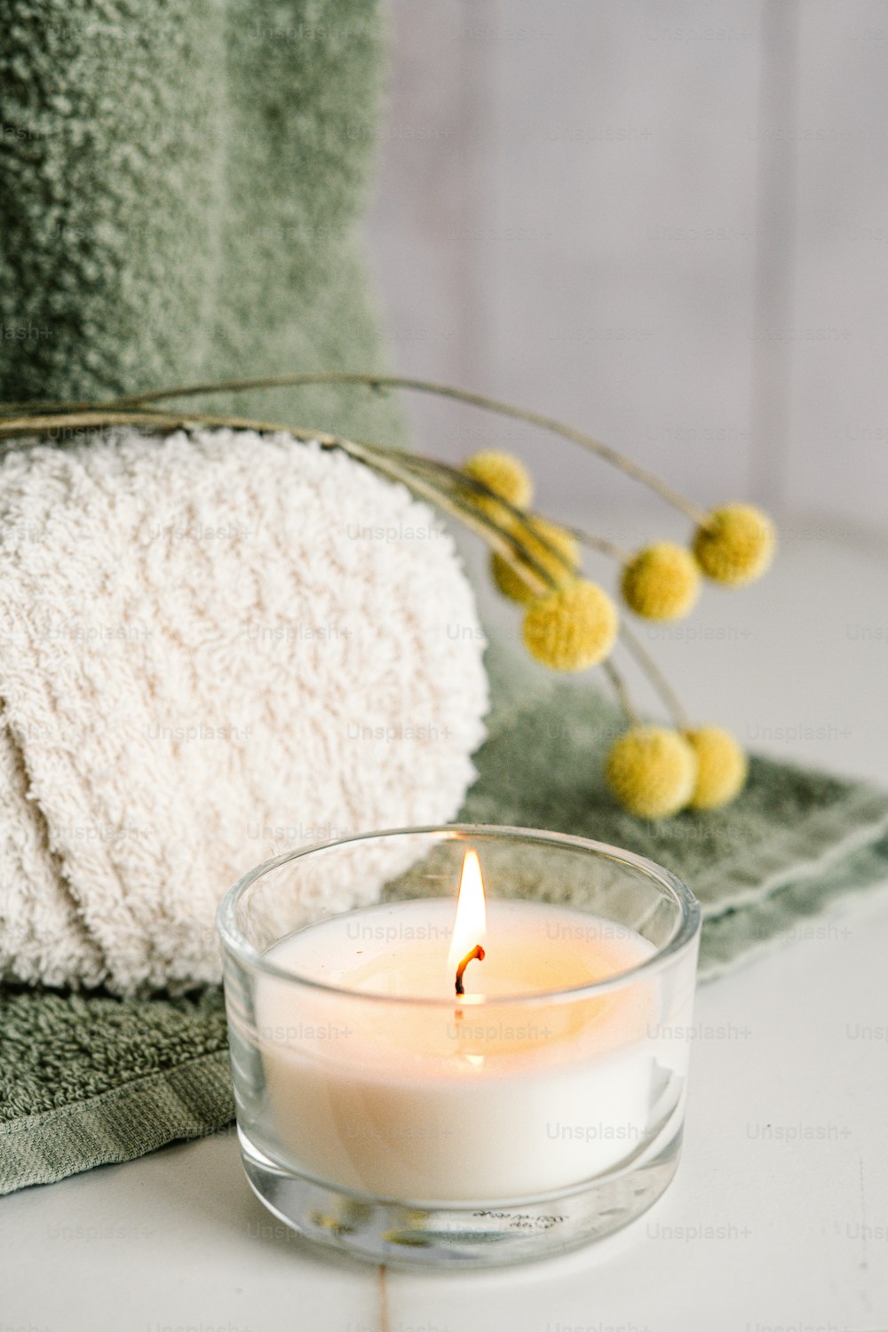 a white candle sitting on top of a table next to a towel