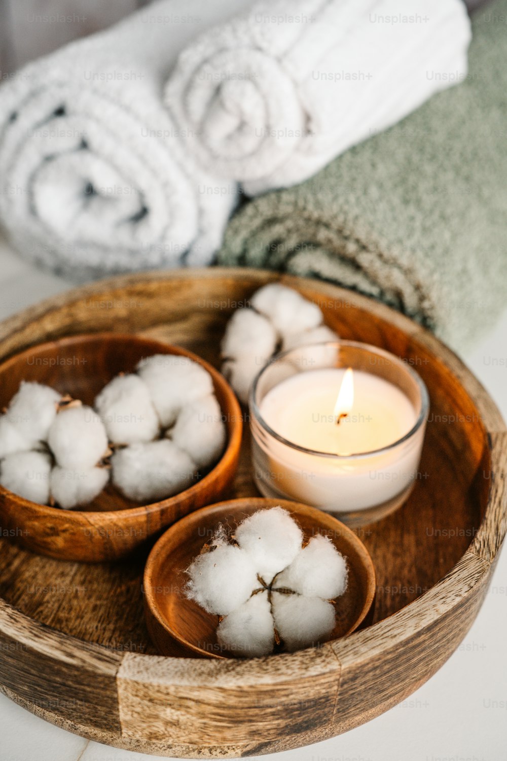 a wooden bowl filled with cotton balls next to a candle