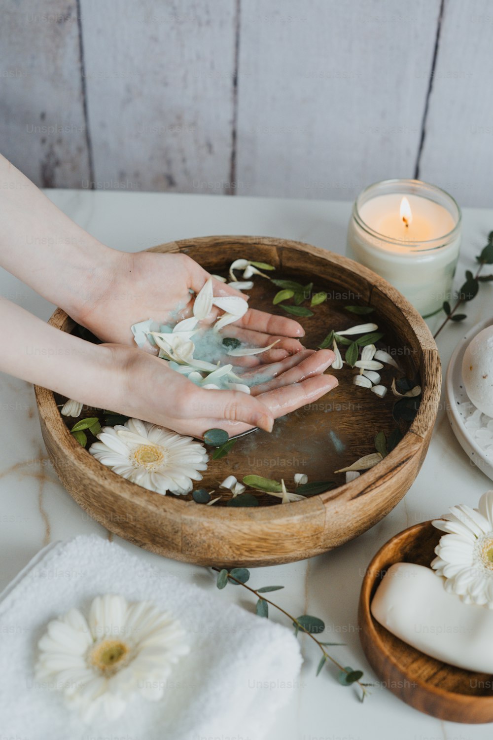 a person's hands on a wooden bowl with flowers and candles