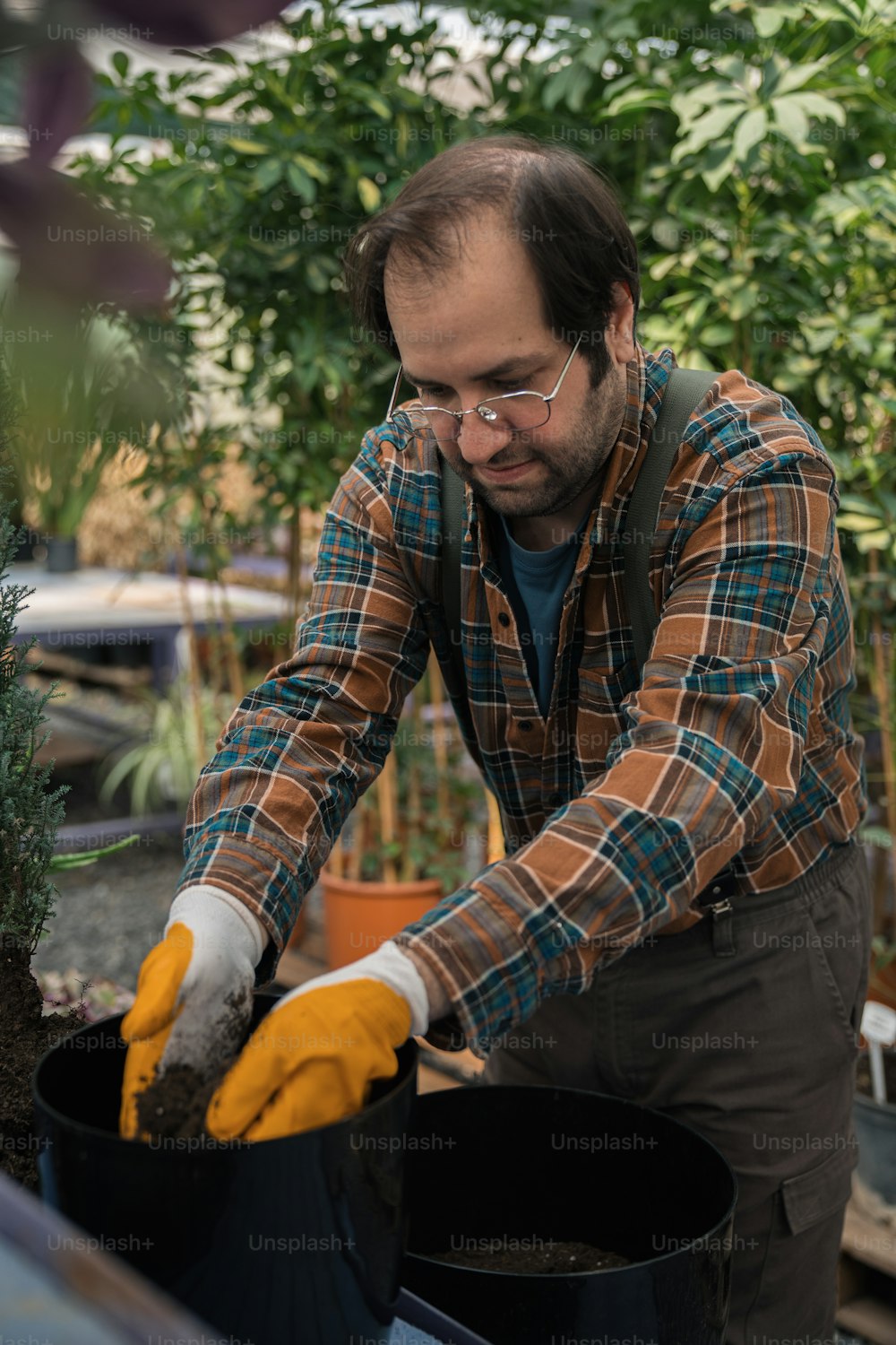 a man in a plaid shirt and yellow gloves working in a greenhouse