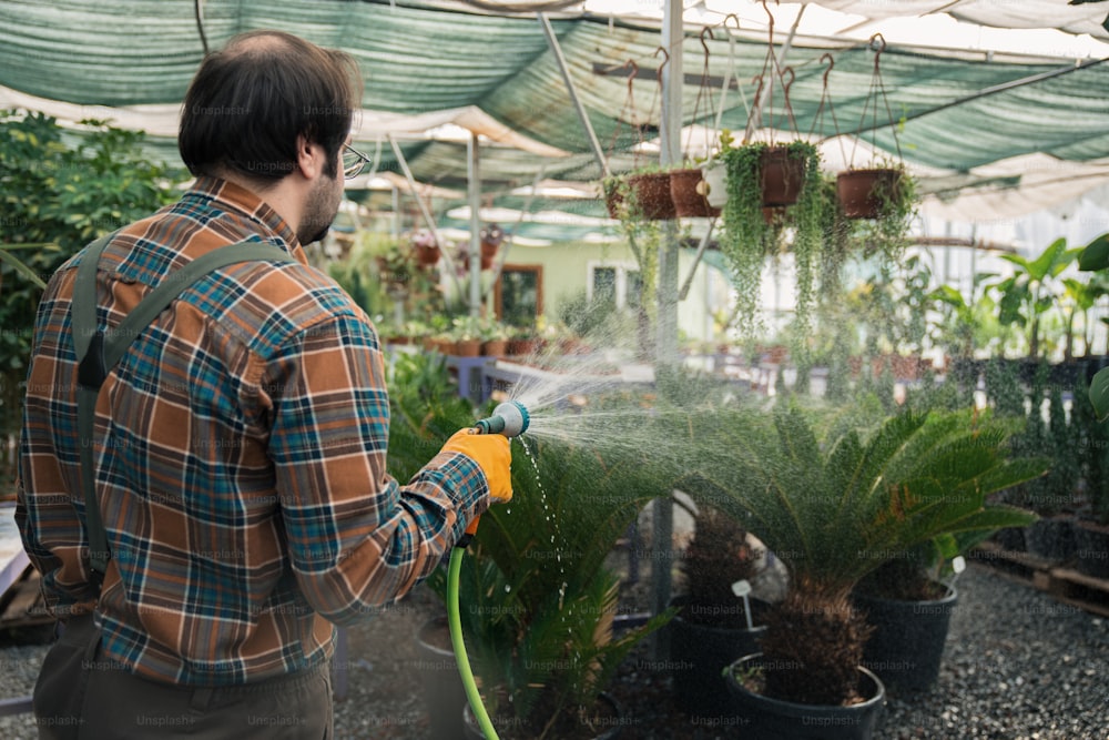 a man watering plants in a greenhouse