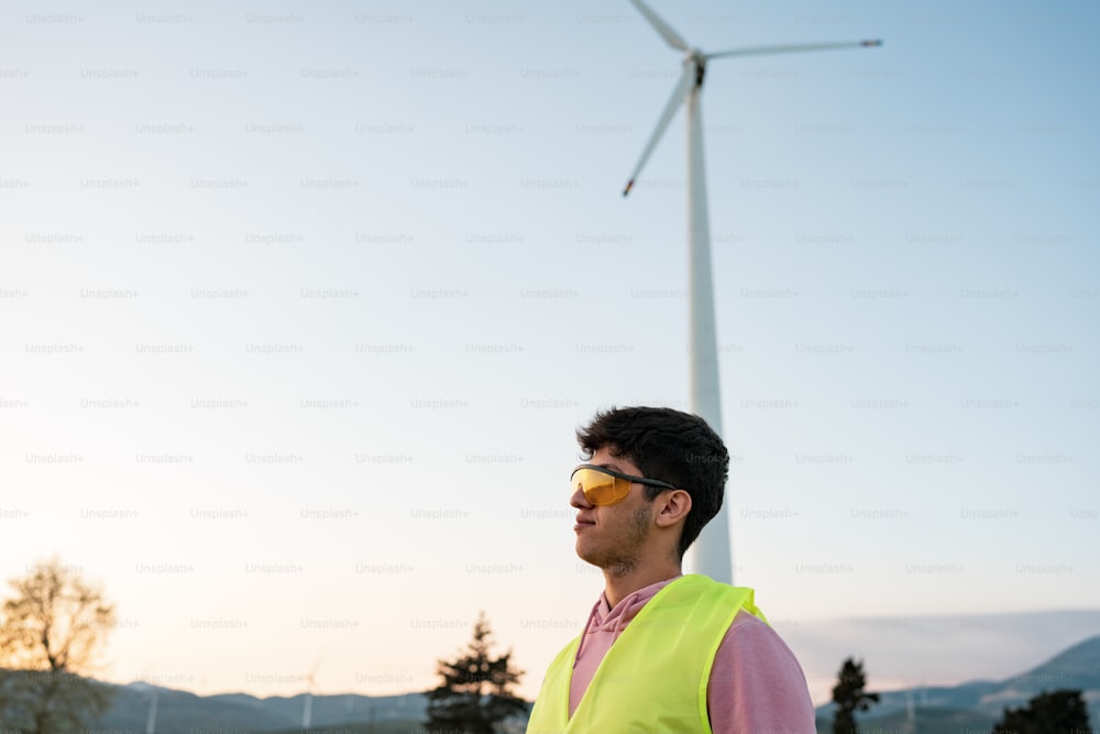 um homem vestindo um colete de segurança em pé na frente de uma turbina eólica