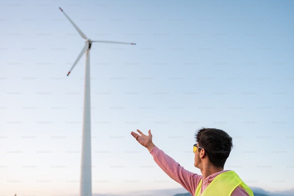 a man in a yellow vest and safety vest standing next to a wind turbine