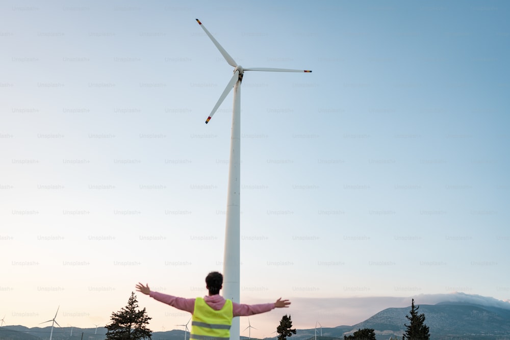 uma pessoa em pé na frente de uma turbina eólica
