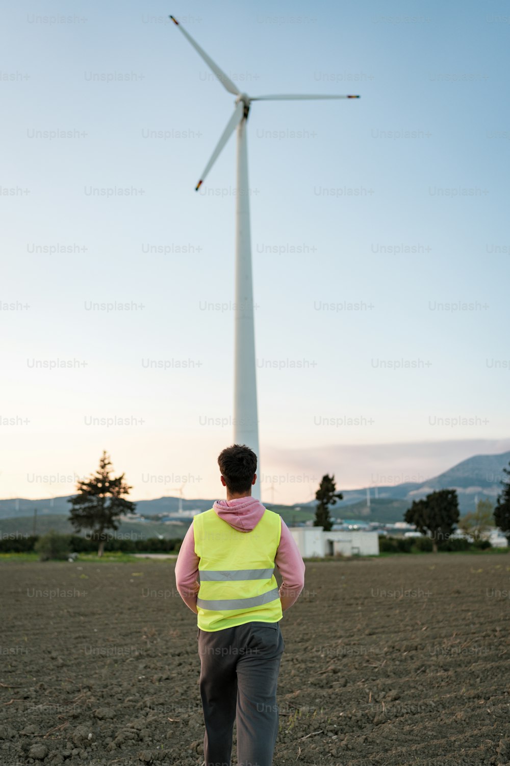 um homem em um colete amarelo em pé na frente de uma turbina eólica