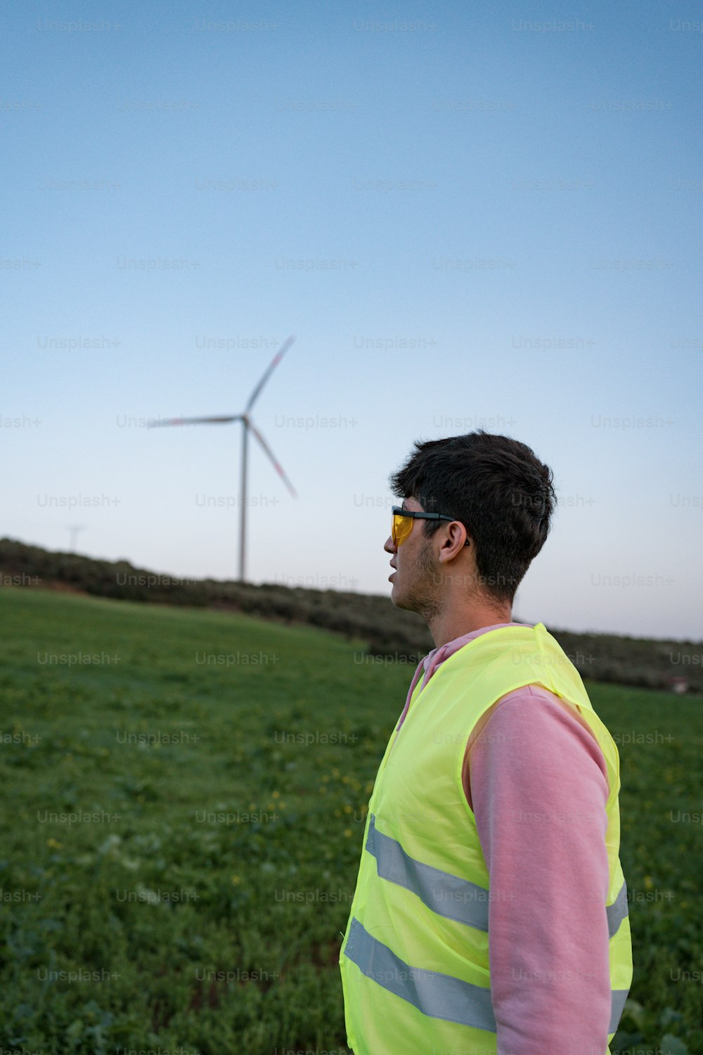 um homem de pé em um campo com uma turbina eólica no fundo