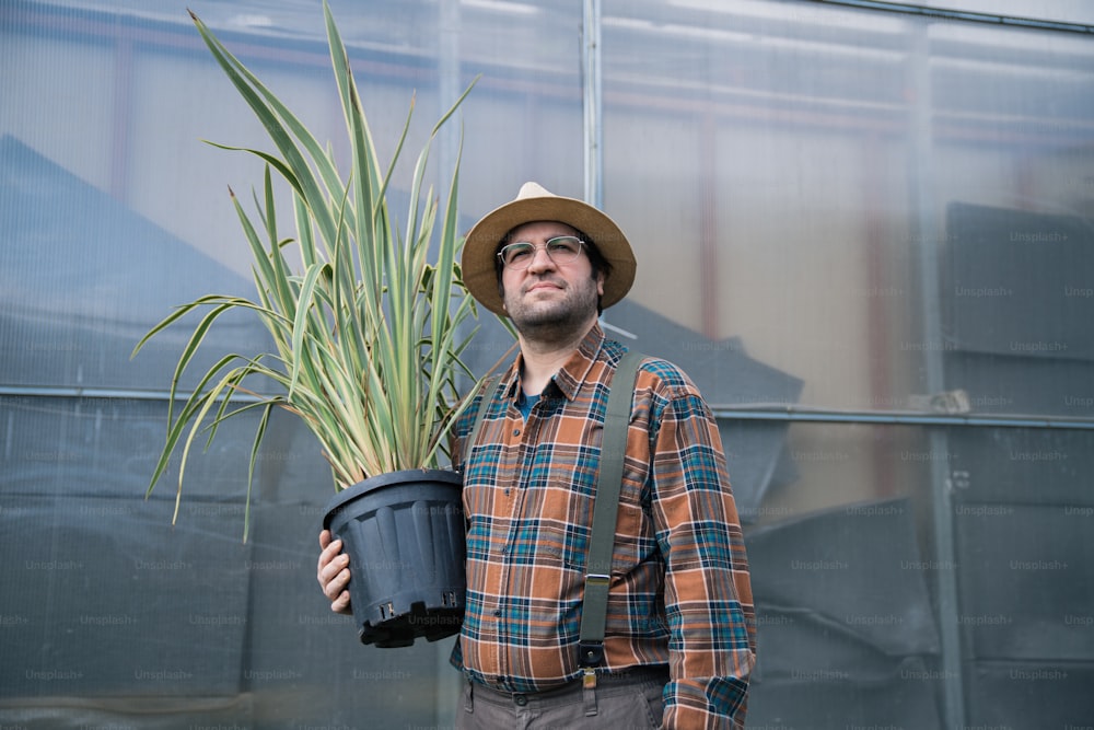 Ein Mann mit Hut, der eine Topfpflanze hält